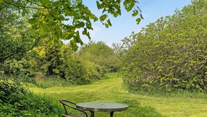 A garden with a round table and wicker chair, surrounded by lush greenery and trees. - Guest Room 'Cocon' with Shared Garden and Wi-Fi (Durtal)