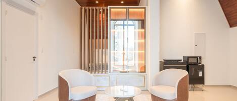 A modern room with two sofas, a small round table, a built-in TV, and a sliding glass door leading to a balcony.