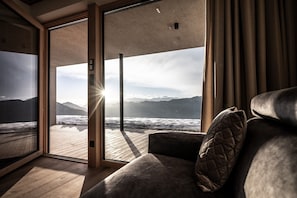 A modern interior with a large sliding glass door leading to a wooden deck overlooking a beach and mountains.