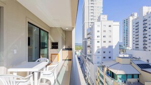 A balcony with a table and chairs, a small kitchen area, and a view of surrounding high-rise buildings. - Apart With Barbecue 600m From the Beach Rgoa701 (Itapema)