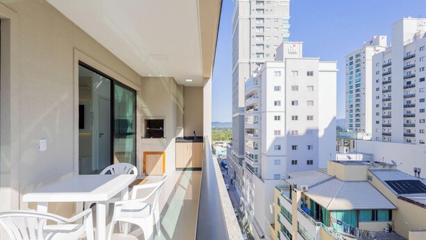 Een balkon met een tafel en stoelen, een kitchenette en uitzicht op omliggende hoogbouw.