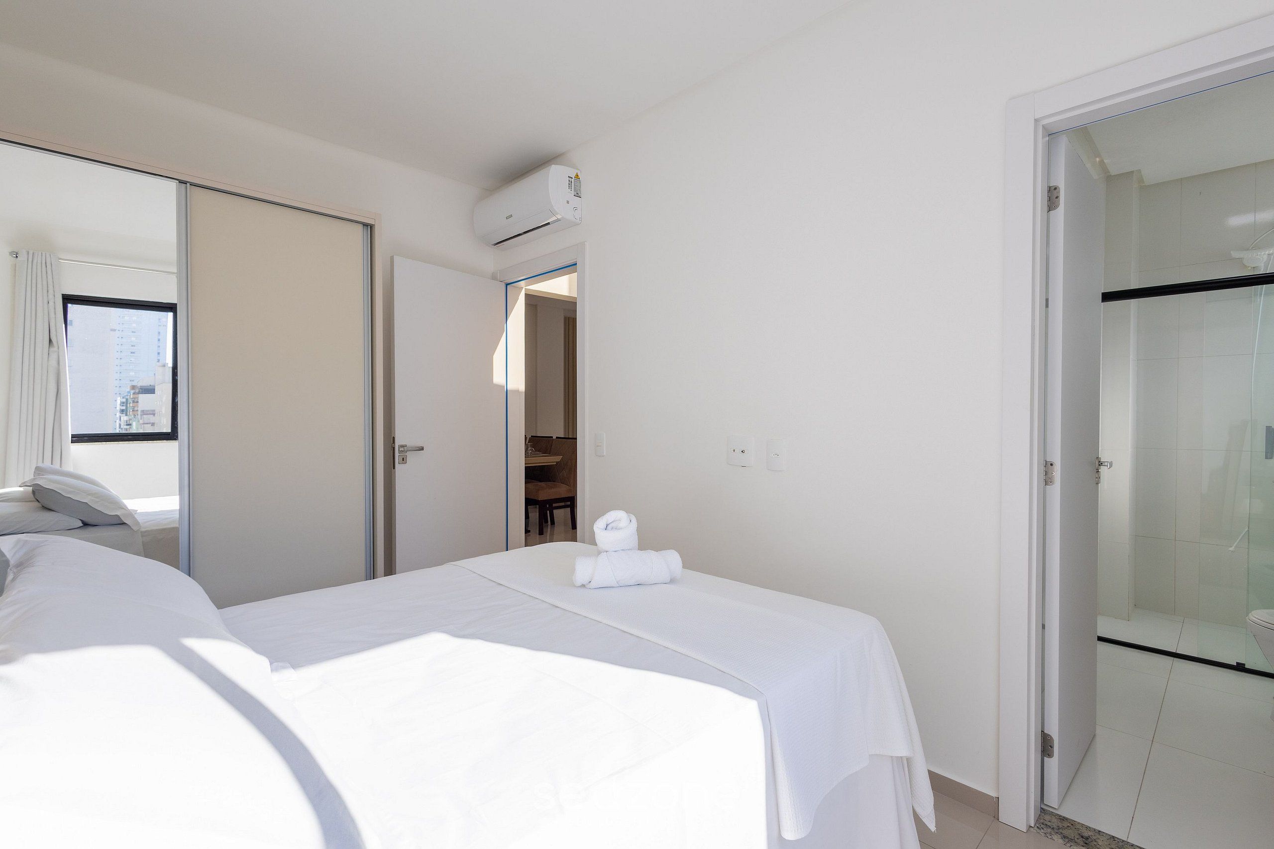 Una habitación de hotel con una cama, un baño con ducha de vidrio y una puerta que da a otra habitación.