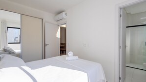 Een hotelkamer met een bed, een badkamer met douchecabine en een deur die naar een andere kamer leidt.