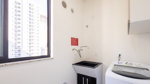 A laundry room with a washing machine, a sink, and a window overlooking a high-rise building. - Apart With Barbecue 600m From the Beach Rgoa701 (Itapema)