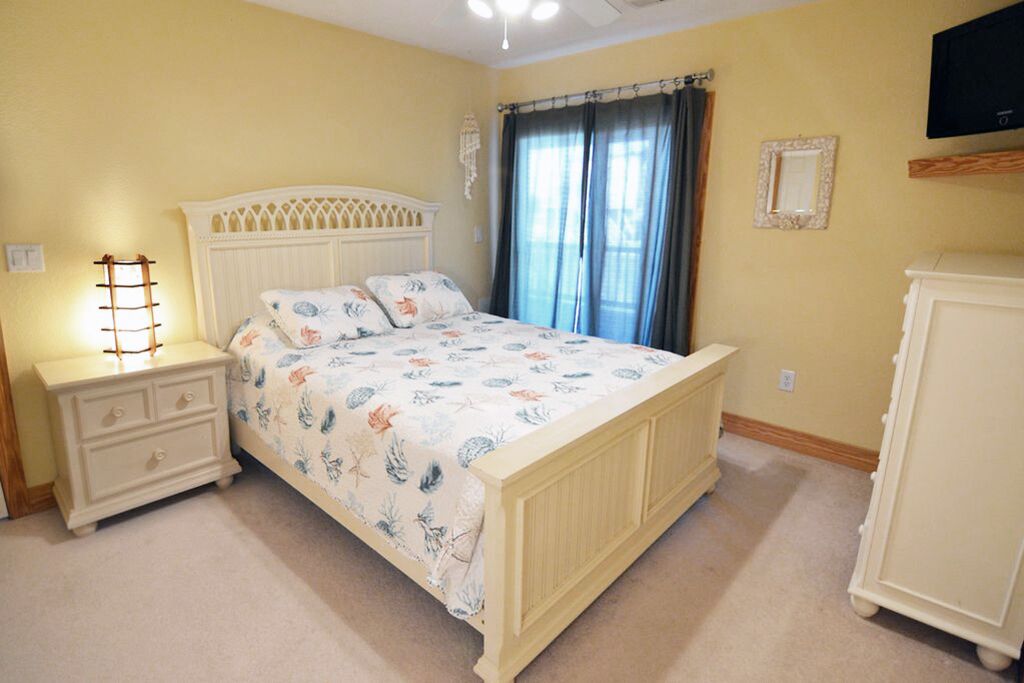 Un dormitorio con cama, mesita de noche, cómoda y televisión en la pared.