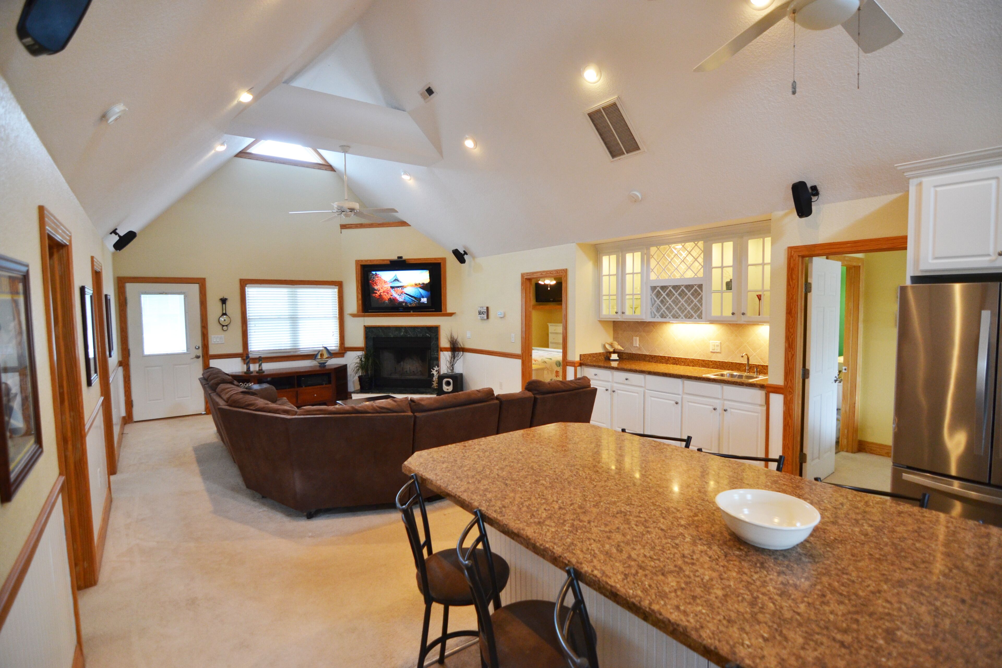 A spacious living area with a large brown sectional sofa, a kitchen with white cabinets, and a built-in fireplace.
