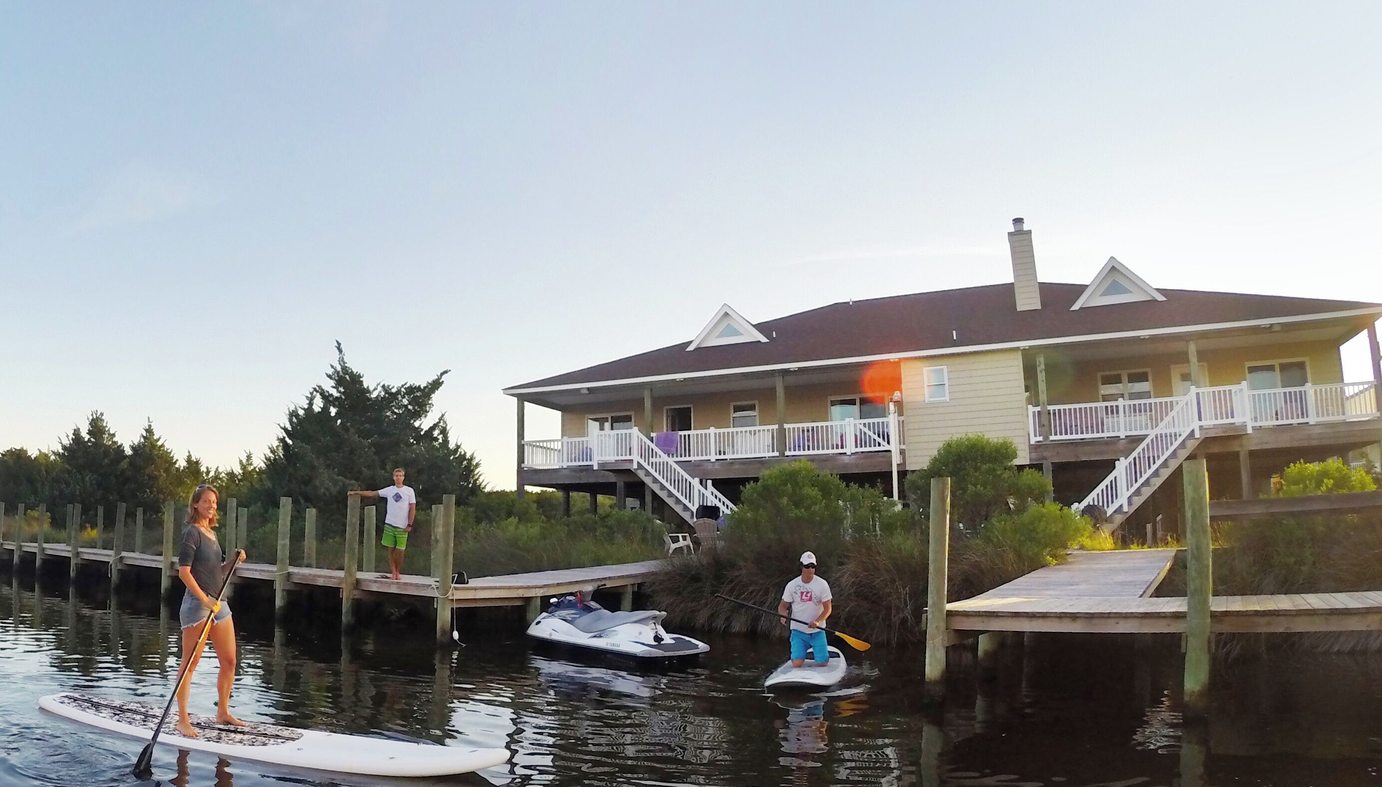 A waterfront property with a dock, paddleboards, and a small boat.