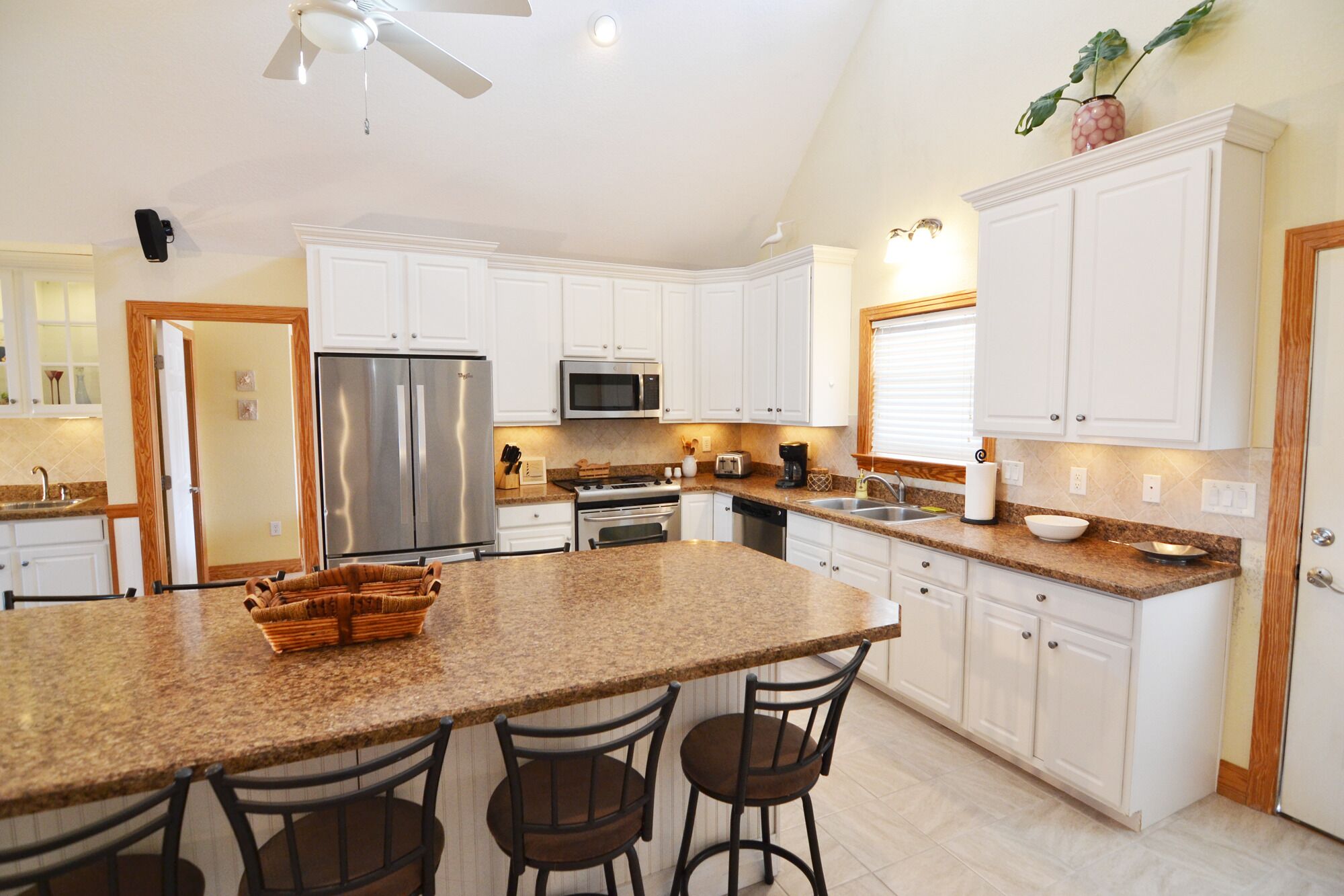 A spacious kitchen with white cabinets, a granite countertop, and a large island with bar stools.