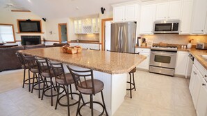 Een moderne keuken met witte kastjes, roestvrijstalen apparatuur en een granieten eiland met barstoelen.