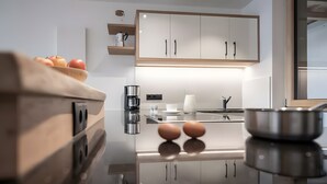 A modern kitchen with a reflective countertop, a coffee maker, and a bowl of fruit.