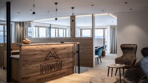 A modern office space with a wooden reception desk labeled 'Leitnerhof Endless Horizon Views,' large windows, and a seating area with chairs.