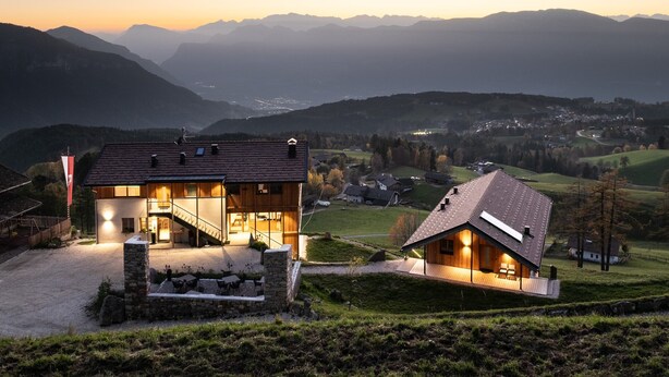 A modern house with a glass facade, a stone staircase, and a view of the surrounding mountains.