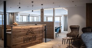 A modern office space with a wooden reception desk labeled 'Leitnerhof Endless Horizon Views,' large windows, and a seating area with chairs.