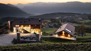 A modern house with a glass facade, a stone staircase, and a view of the surrounding mountains.