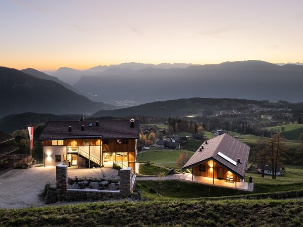 A modern house with a glass facade, a stone staircase, and a view of the surrounding mountains.