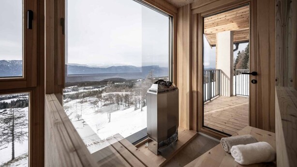 A wooden cabin with a large window, a fireplace, and a balcony.
