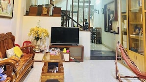 Una sala de estar moderna con televisor, muebles de madera, ventilador de techo y una escalera que sube a un nivel superior.