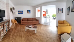 A spacious living room with a wooden floor, a brown sofa, a yellow armchair, and a television on a wooden cabinet. - La Petit Alonnaise - Charming seaside house (Châtelaillon-Plage)