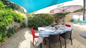 Une terrasse extérieure avec une table dressée pour le repas, entourée d’une végétation luxuriante et protégée par un auvent bleu.