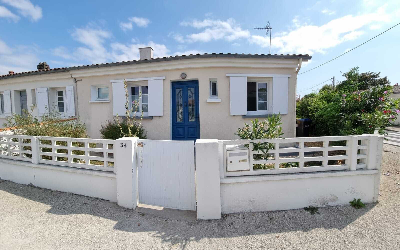 Ein eingeschossiges Gebäude mit einer blauen Tür, weißen Fensterläden und einem weißen Zaun.