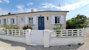 Un bâtiment d’un seul étage avec une porte bleue, des volets blancs et une clôture blanche.
