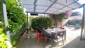 Une terrasse extérieure avec une table et des chaises, entourée de verdure et dotée d’un espace abrité.