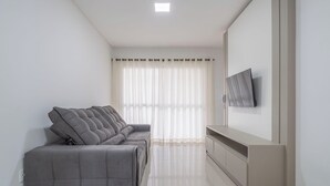 A modern living room with a sofa set, a flat-screen TV mounted on the wall, and a window with sheer curtains. - Apt w/ Balcony & Bbq, 650m to Beach Rgo0502 (Itapema)