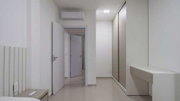 A modern, minimalist hallway with a built-in air conditioning unit, a door leading to another room, and a small bedside table with a remote control. - Apt w/ Balcony & Bbq, 650m to Beach Rgo0502 (Itapema)