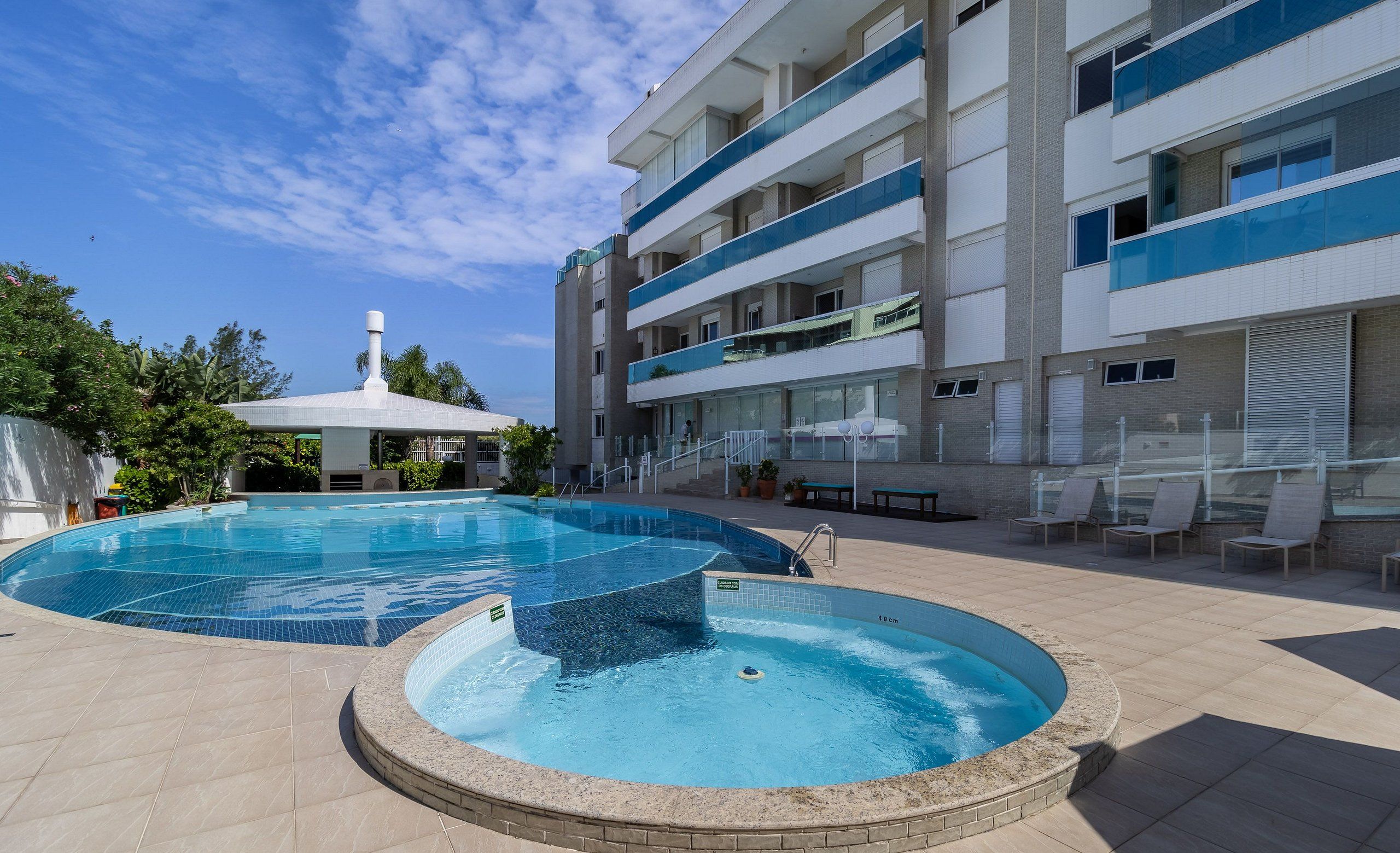 Ett poolområde med en rund bubbelpool, en överbyggd sittgrupp och en flervåningsbyggnad med balkonger.