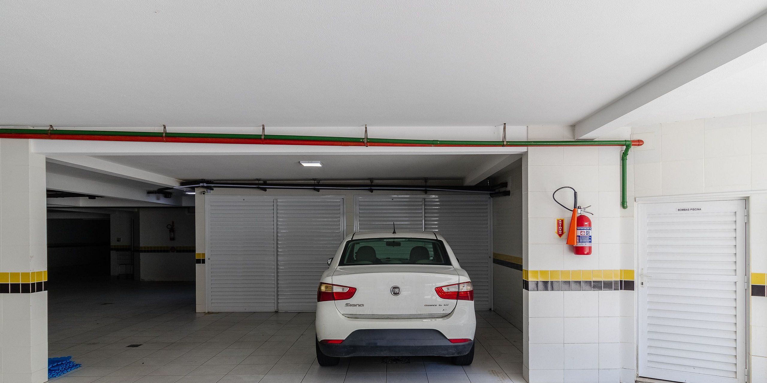 Un coche blanco aparcado en un garaje con un extintor colgado en la pared.