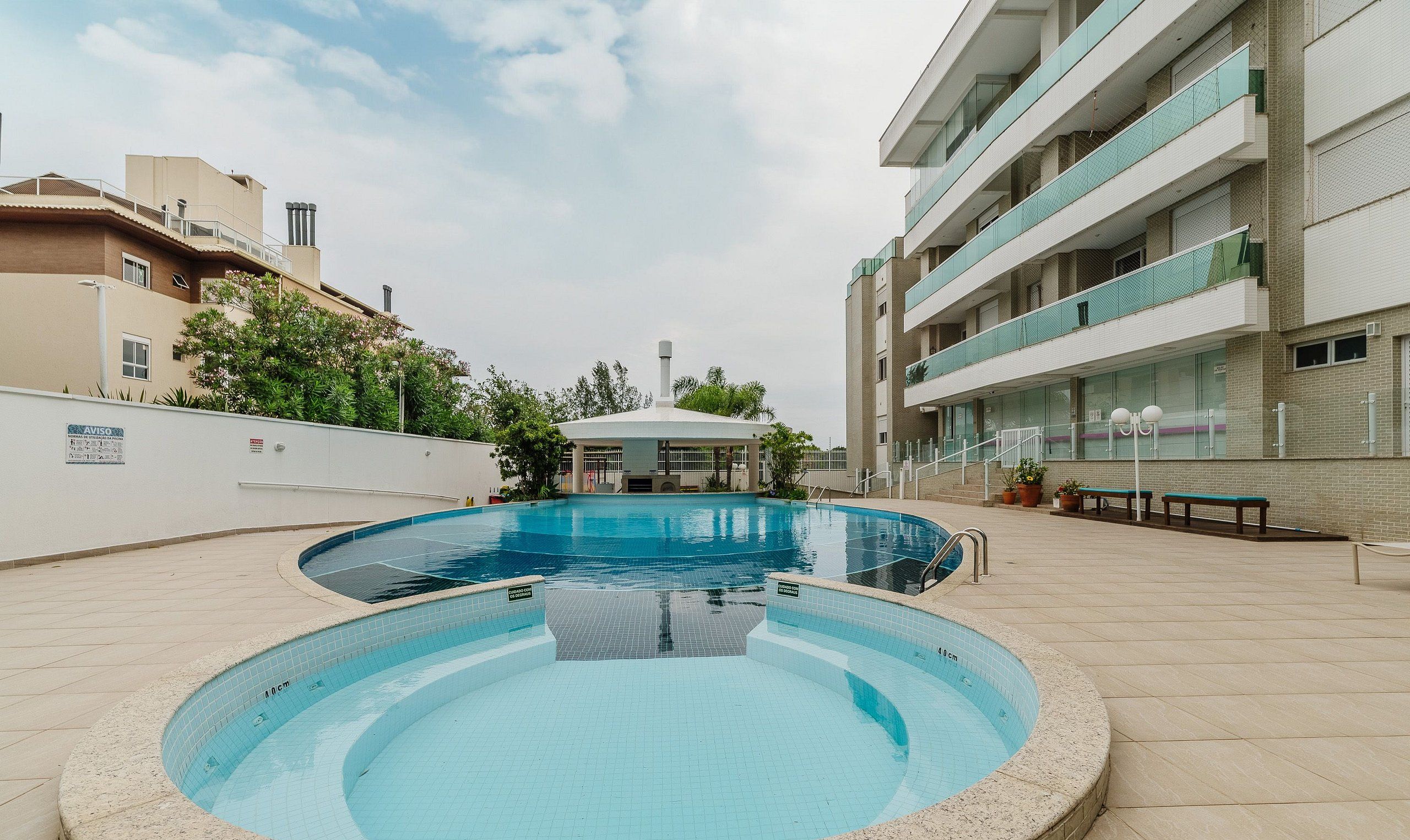 Una piscina con zona cubierta, rodeada por un edificio de varios pisos con balcones.