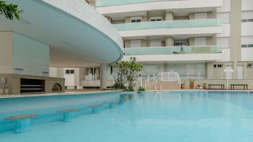 Una piscina con un edificio curvo al fondo, varios balcones y plantas en macetas.