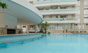 A swimming pool with a curved building in the background, multiple balconies, and potted plants. - Apt w/ Side sea View, Seaside Condominium Rap0306 (Florianópolis)