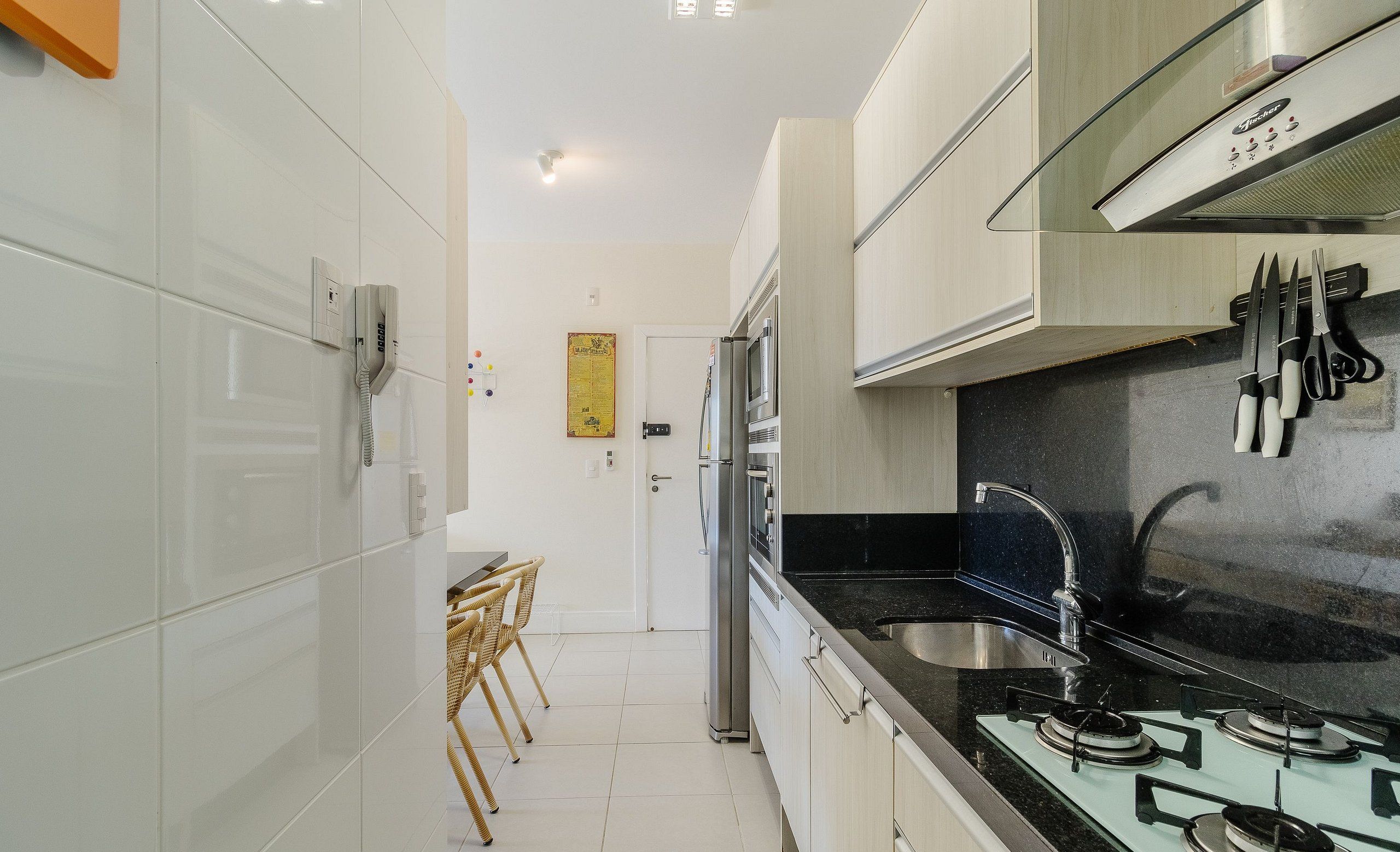 Una cocina moderna con armarios blancos, encimera negra y electrodomésticos de acero inoxidable. Se distingue un área de comedor con una mesa y sillas al fondo.