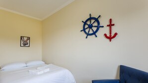 A hotel room with a bed, a blue armchair, and nautical-themed wall decor. - Beautiful Apt With BBQ 850m From the Beach Ral204 (Florianópolis)