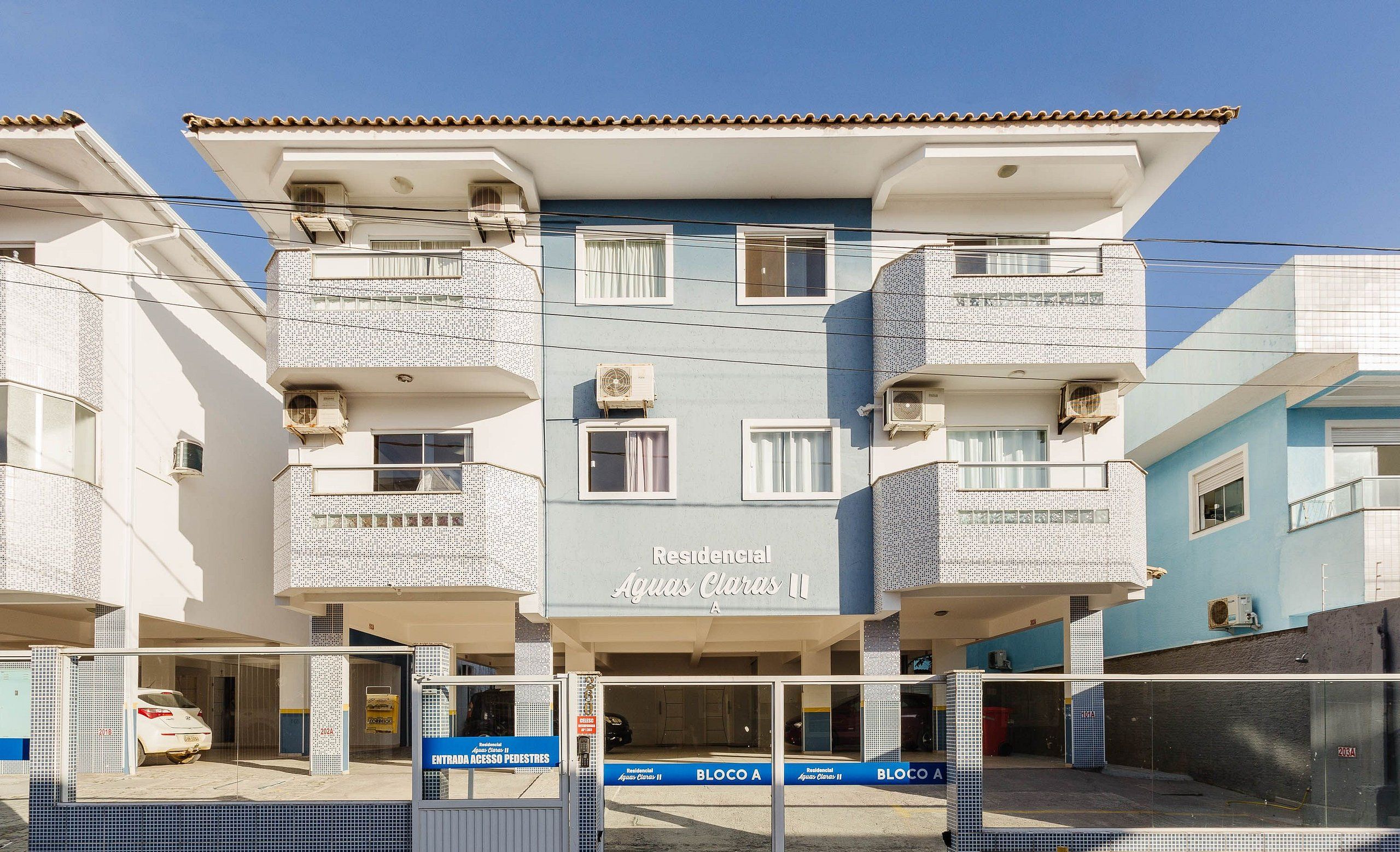 Edifício residencial chamado 'Aguas Claras II' com várias varandas, aparelhos de ar condicionado e entrada com portão.
