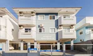 Edifício residencial chamado 'Aguas Claras II' com várias varandas, aparelhos de ar condicionado e entrada com portão.