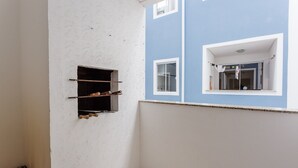 Un rincón de una habitación con una pared blanca con textura, una pared azul con una ventana y un estante con objetos.