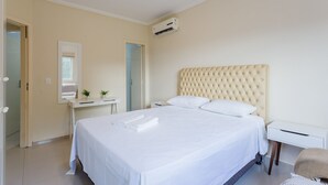 Un dormitorio ordenado con una cama grande, una mesita de noche, un escritorio pequeño y un equipo de aire acondicionado.
