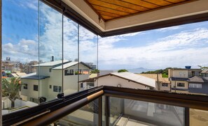 A balcony with a glass railing overlooking a residential area with houses and a clear sky.