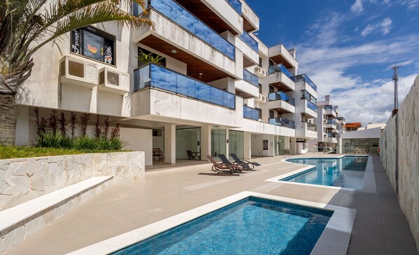 A modern building with multiple balconies, a swimming pool area, and outdoor seating.