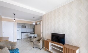 A modern living room with a TV, sofa, and armchair. A kitchen is visible in the background.