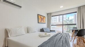 Ein Hotelzimmer mit Bett, einem grauen Sessel, einem kleinen Tisch und einem Fenster mit Blick auf Gebäude.