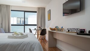 Una habitación de hotel con cama, escritorio, televisión y ventana con cortinas.