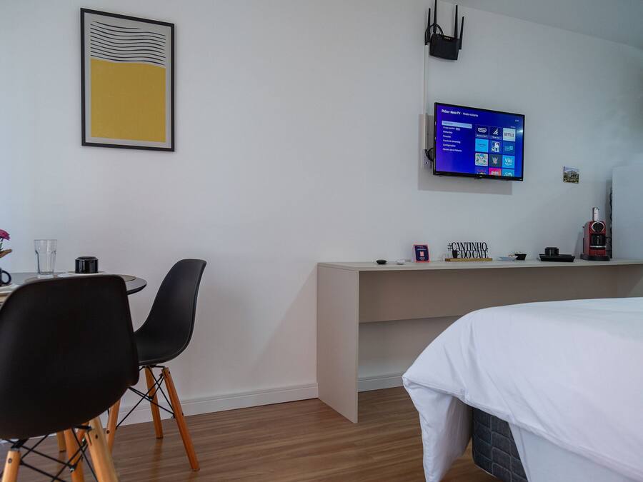 A hotel room with a bed, a desk, a chair, a TV mounted on the wall, and a framed picture on the wall.