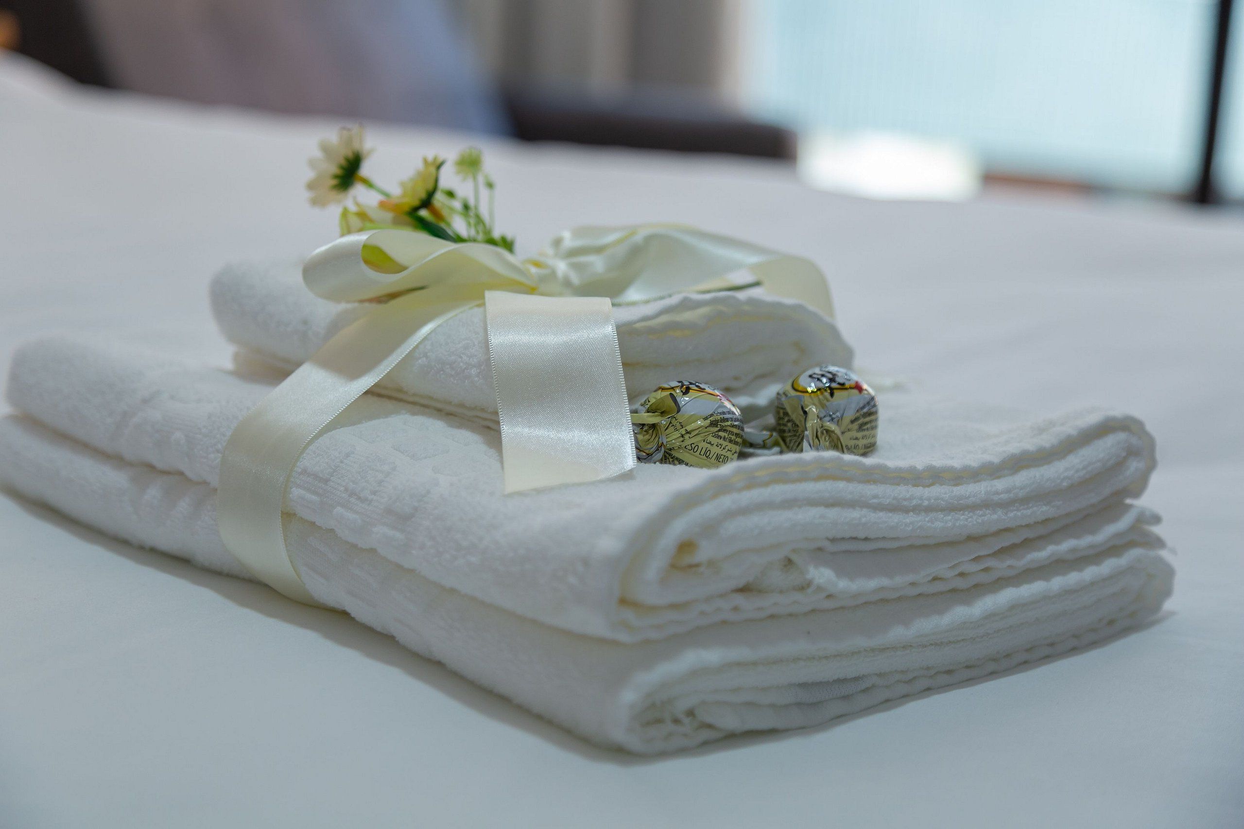 A neatly folded white towel with a ribbon and a small decorative item on a white surface.