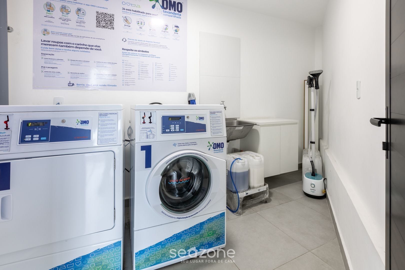 A laundry room with two OMO washing machines, a drying machine, and a vacuum cleaner.