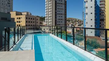 Una piscina en la azotea con barandilla de vidrio, rodeada de edificios altos.