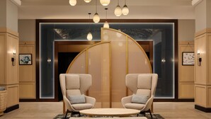 A lobby with a round seating area, hanging pendant lights, and a wall with a tree mural.