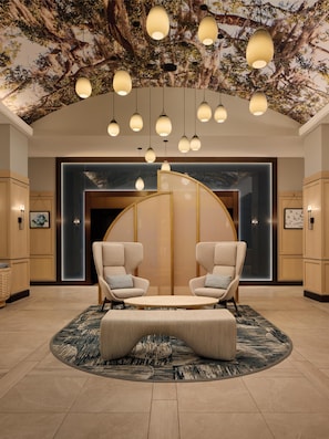 Un hall dâentrĂ©e dotĂ© dâun espace salon circulaire, de luminaires suspendus et dâun mur ornĂ© dâune fresque reprĂ©sentant un arbre.
